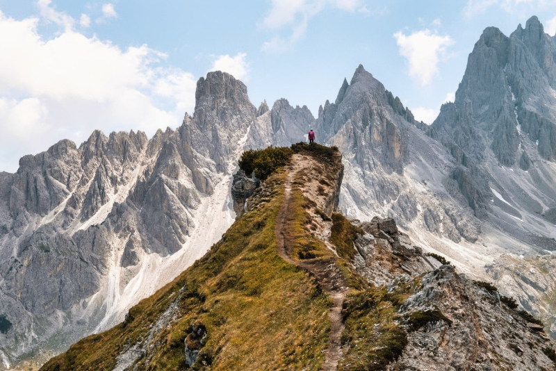 Hiker on a dramatic ridge on the Alta Via 1 trail in the Dolomites, Italy, with jagged peaks and scree slopes in the background