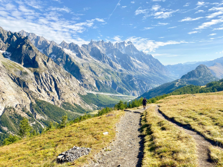 Hiker on a mountain trail with the Mont Blanc massif and jagged Alpine peaks in the background on the Tour du Mont Blanc route