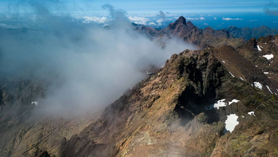 Dramatic aerial view of the GR20 trail ridge in Corsica, France, with granite peaks and low cloud
