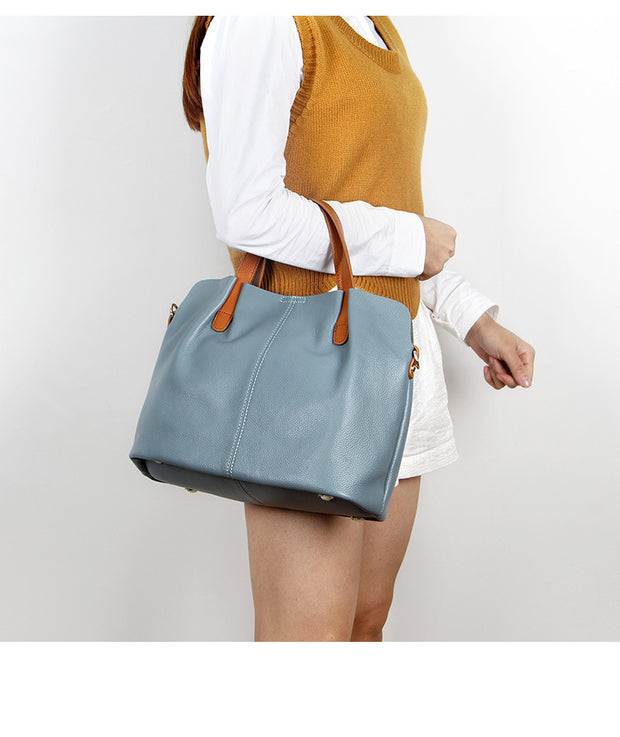 Woman holding blue leather tote bag with brown handles